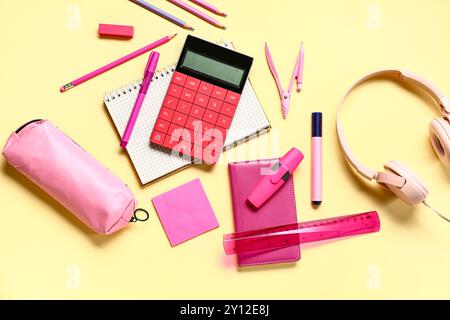 Modern calculator with headphones and different stationery on pale yellow background Stock Photo