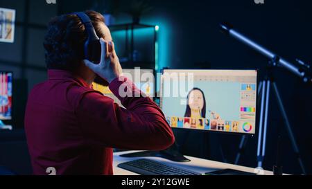 Photographer in creative studio working on digital portfolio showcasing photoshoot edited images. Photo editor selecting best photographs while listening music in headphones Stock Photo