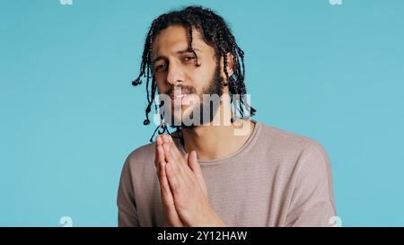 Desperate guy asking for forgiveness, putting hands together in imploring gesturing, showing regret emotion. Upset man saying sorry, begging for apology, feeling guilty, studio background, camera B Stock Photo