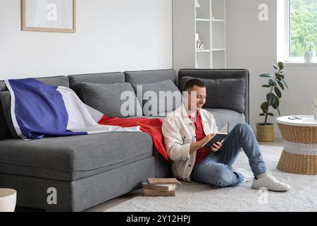 Young man with flag of France reading book at home Stock Photo