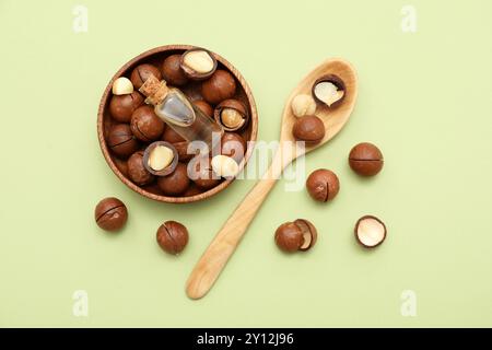 Bottle of macadamia oil and nuts in bowl on green background Stock Photo