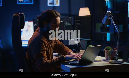 Computer scientist putting headphones on while developing code on PC, making time pass faster during remote job shift. IT admin doing multitasking in home office while listening music, camera A Stock Photo