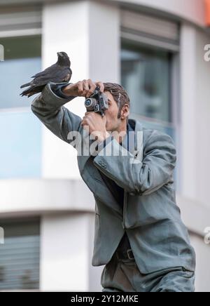 Echte Krähe auf einem Säulenheiligen, Der Fotograf, vor dem Hauptbahnhof in Düsseldorf, eine von 10 realistischen, lebensgroßen Skulpturen von Menschen auf Litfaßsäulen, vom Düsseldorfer Künstler Christoph Pöggeler, Kunst im Öffentlichen Raum, NRW, Deutschland, Säulenheililge Kunstprojekt *** Real crow on a pillar saint, The photographer, in front of the main station in Düsseldorf, one of 10 realistic, life-size sculptures of people on advertising pillars, by Düsseldorf artist Christoph Pöggeler, art in public space, NRW, Germany, pillar saint art project Stock Photo