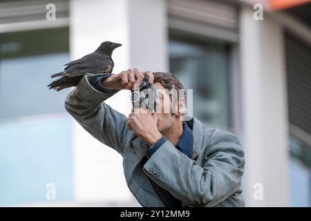 Echte Krähe auf einem Säulenheiligen, Der Fotograf, vor dem Hauptbahnhof in Düsseldorf, eine von 10 realistischen, lebensgroßen Skulpturen von Menschen auf Litfaßsäulen, vom Düsseldorfer Künstler Christoph Pöggeler, Kunst im Öffentlichen Raum, NRW, Deutschland, Säulenheililge Kunstprojekt *** Real crow on a pillar saint, The photographer, in front of the main station in Düsseldorf, one of 10 realistic, life-size sculptures of people on advertising pillars, by Düsseldorf artist Christoph Pöggeler, art in public space, NRW, Germany, pillar saint art project Stock Photo