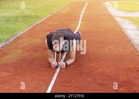 Young man doing plank exercise in the morning outdoor on the running race track Stock Photo