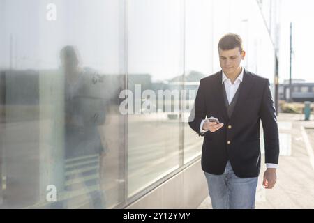 Young and Casual Businessman Using Smartphone while Walking Outside of Office Building Stock Photo