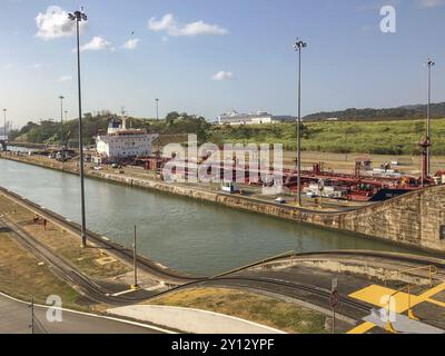 Scene in an industrial area with a large ship in the canal surrounded by containers and buildings. The sky is clear, panama city, panamakanl, panama, Stock Photo