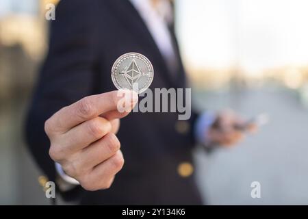 Ethereum cryptocurrency coin in a young businessman hand. Disruptive blockchain technology concept and transfer of wealth Stock Photo