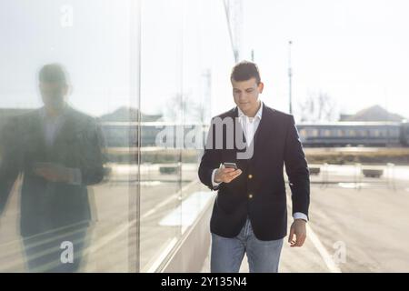 Young and Casual Businessman Using Smartphone while Walking Outside of Office Building Stock Photo