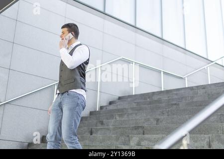 Young and Casual Businessman Using Smartphone while Walking Outside of Office Building Stock Photo