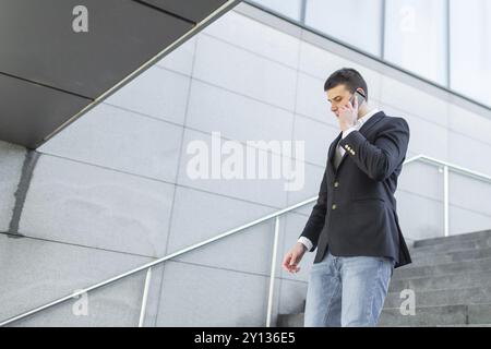 Young and Casual Businessman Using Smartphone while Walking Outside of Office Building Stock Photo