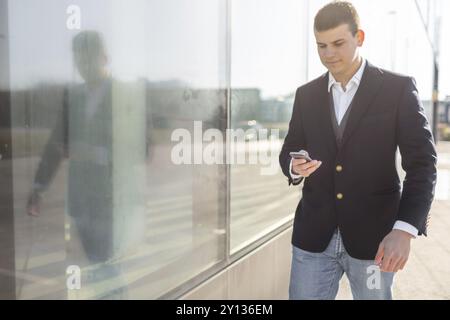 Young and Casual Businessman Using Smartphone while Walking Outside of Office Building Stock Photo
