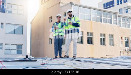 Business people, electrician and discussion with tablet on rooftop for building maintenance or installation in city. Contractor, electrical engineer Stock Photo