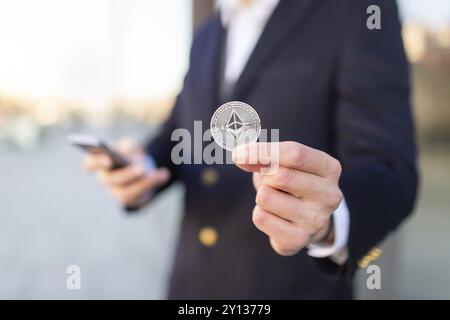 Ethereum cryptocurrency coin in a young businessman hand. Disruptive blockchain technology concept and transfer of wealth Stock Photo