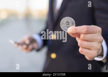 Ethereum cryptocurrency coin in a young businessman hand. Disruptive blockchain technology concept and transfer of wealth Stock Photo