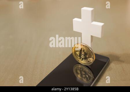 Dead Bitcoin concept with white cross and smartphone as grave Stock Photo