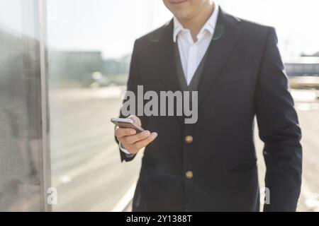Young and Casual Businessman Using Smartphone while Walking Outside of Office Building Stock Photo