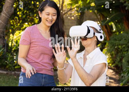 Using VR headset, asian grandmother exploring virtual reality with daughter outdoors Stock Photo