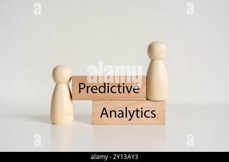 Two wooden figures are stacked on top of each other with the word predictive analytics written below them Stock Photo