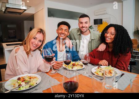 Portrait of a group of multiracial young friends having a lunch and eating together, enjoying a salad. Two multiethnic couples looking at the camera while having a healthy vegetarian dinner at home. High quality photo Stock Photo