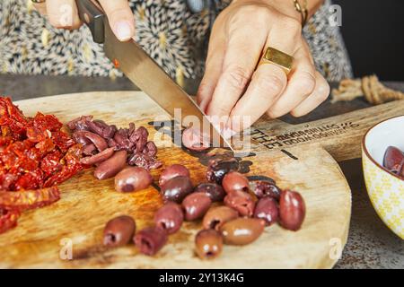 Close-up of hands cutting olives, sun-dried tomatoes and other ingredients on wooden cutting boards in a kitchen. Stock Photo