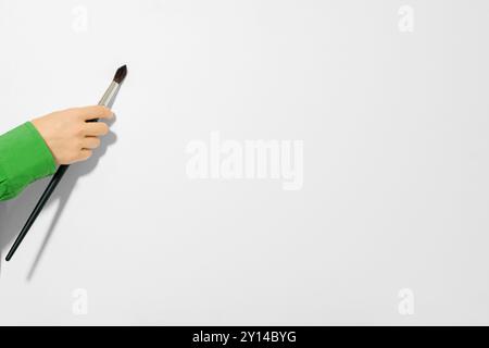 Female hand touching white canvas with brush, close up. Artist hand with one brush on white background Stock Photo