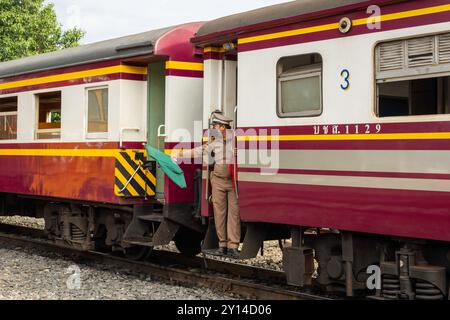 Thailand. 31st Aug, 2024. A train station officer is seen waving a green flag as a safe signal, at the door of a train, in Nakhon Pathom province, in Thailand. Nakhon Pathom province, west of Bangkok, is one of Thailand's oldest cities, with fertile lands supporting a variety of crops, including rice, coconuts, and sugarcane, making agriculture a vital part of the local economy. Credit: SOPA Images Limited/Alamy Live News Stock Photo