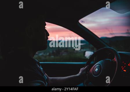 a man driving a car into a beautiful landscape at sunset Stock Photo