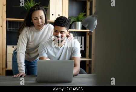 Happy interracial couple smiling while working or having fun at laptop Stock Photo
