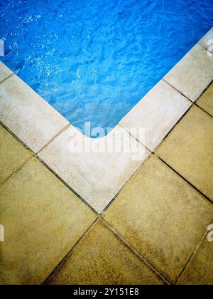 A close-up of a swimming pool corner showcasing textured tiles and clear water in bright daylight Stock Photo