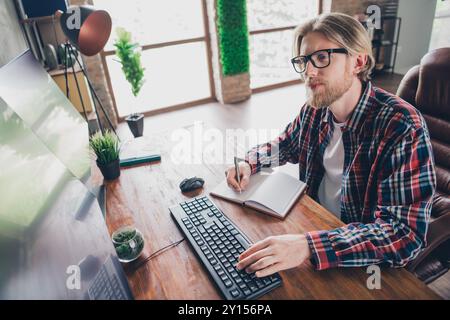 Photo of nice young male work study computer write notebook wear plaid shirt modern office loft room interior indoors businessman workspace Stock Photo