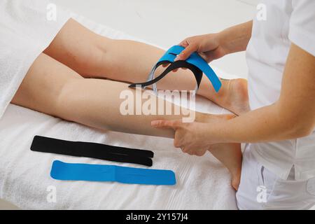 Kinesio taping of the lower extremities to prolong the massage effect close-up, the therapist applies tape to the patient's legs Stock Photo