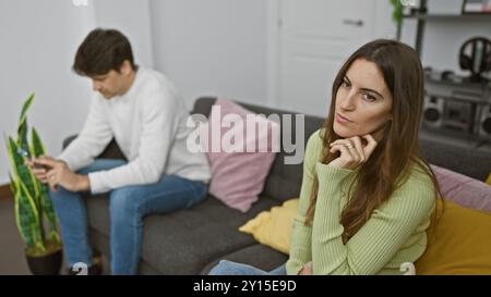 A woman and a man, seemingly in a relationship, appear disconnected in a modern living room. Stock Photo