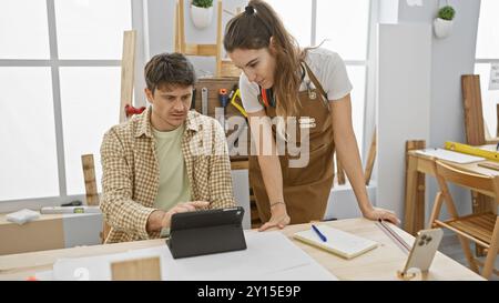 Man and woman collaborating in a bright carpentry workshop, analyzing plans on a tablet. Stock Photo