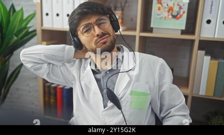 Young arab man with beard wearing headphones in clinic office relaxing during break Stock Photo