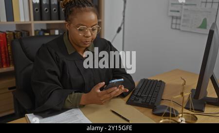 Woman judge using smartphone at desk in office with computer keyboard and legal documents on workspace Stock Photo