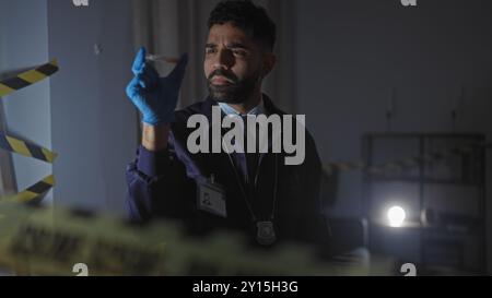 Hispanic detective examines evidence at an indoor crime scene with focus and seriousness. Stock Photo