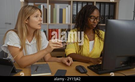 Women working together at an office desk with a computer, discussing a project in a modern workplace interior. Stock Photo