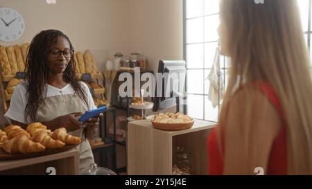 Waitress using a tablet to take an order from a customer in a cozy bakery filled with bread and pastries. Stock Photo