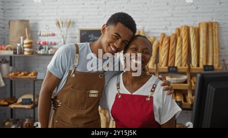 Bakers working together in a bakery room with shelves of fresh bread, featuring a smiling man and woman in aprons indoors Stock Photo