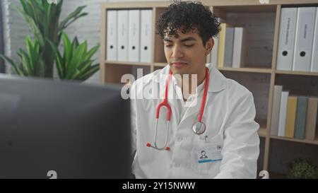 A focused hispanic man in a lab coat examines a computer in a clinical setting, embodying a professional and attentive medical practitioner. Stock Photo
