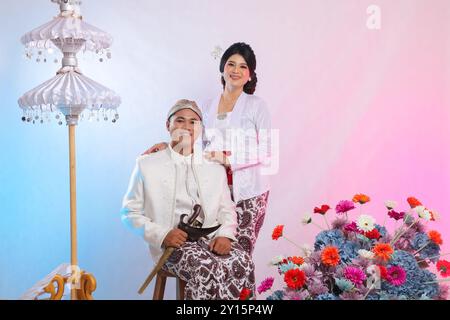 couple of man and woman lovers, cheerful young Asian man sitting carrying a keris next to his woman who is wearing modern Javanese traditional clothin Stock Photo