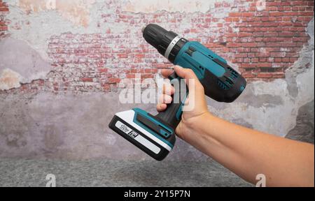 Electric turquoise power drill in hand against a brick wall. Stock Photo