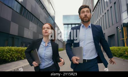 Caucasian businesspeople business colleagues coworkers partners managers businesswoman businessman walking in city talking check time look at writ Stock Photo