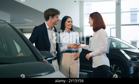 Caucasian couple clients buyers conclude agreement deal buy buying new car auto automobile in showroom rental service rent transport shaking hands Stock Photo