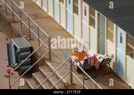 One Person Relaxing On Folding Chairs Next to A Table Outside A Beach Hut On Sidmouth Beach, Sidmouth UK Stock Photo