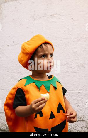 Boy dressed as a pumpkin eats a treat on halloween day. Stock Photo