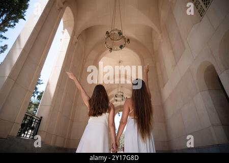 Two women in white dresses stand in an arched doorway, one with her arm raised. They face away from the camera, looking up at a chandelier. Stock Photo