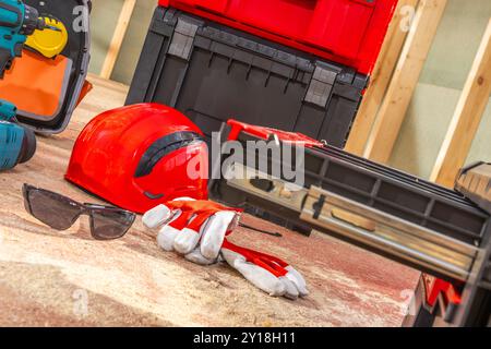 Various construction tools and safety equipment are arranged on the ground, including a hard hat, safety glasses, gloves, and toolboxes, ready for ren Stock Photo