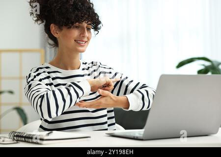 Young woman using sign language for communication during video call at white table indoors Stock Photo